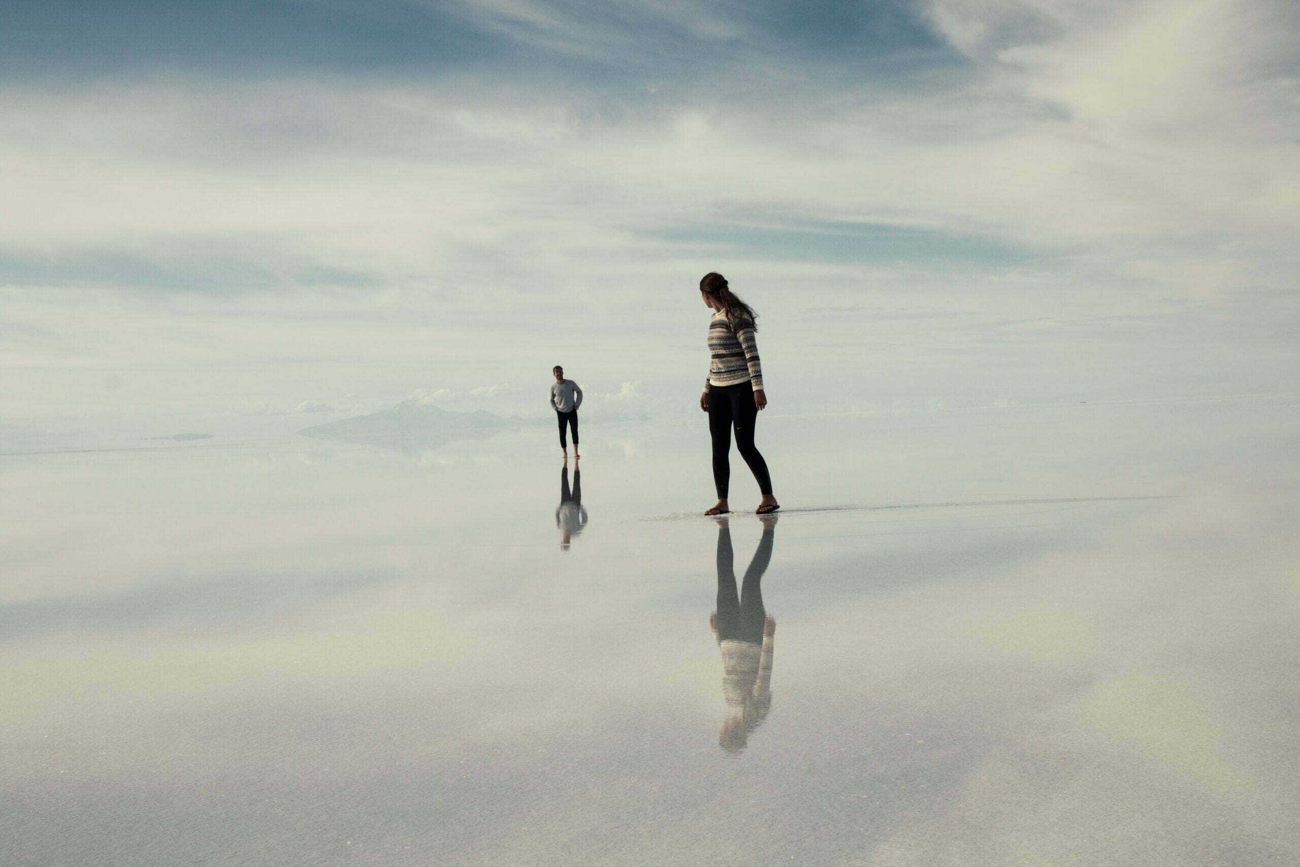 two people on beach with wet sand reflecting clouds above for mindset in business article