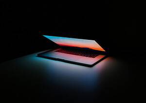 black laptop with blue and red screen glowing against black background for simple crm article
