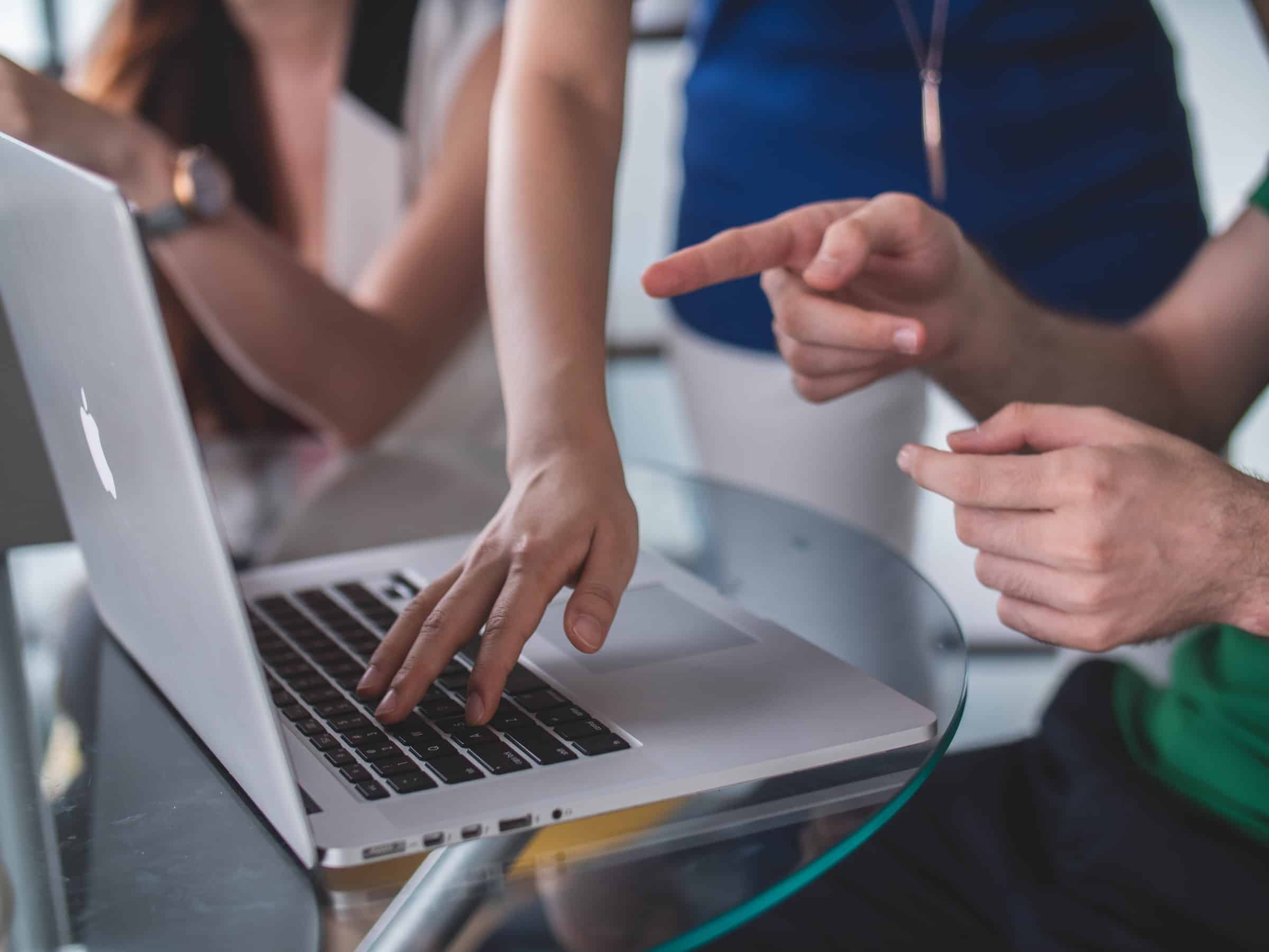 person touching macbook pro keyboard while another person points at macbook for small business crm article